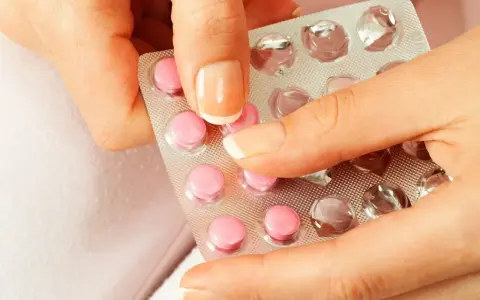 Dłonie trzymające blister z różowymi tabletkami. Wybór najlepszej antykoncepcji bez tycia to ważna decyzja.