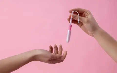 Dwie dłonie, jedna trzyma tampon z aplikatorem, druga wyciągnięta do przyjęcia. Ciasna pochwa to temat, który wymaga dyskrecji.