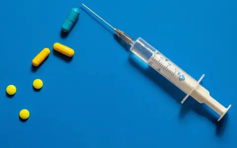 Strzykawka z igłą i kilka tabletek, w tym kapsułki. Może to być przygotowanie do zastrzyku hormonalnego.