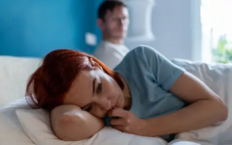 Zamyślona kobieta z rudymi włosami leży w łóżku, zastanawiając się: "czy jestem toksyczna?". W tle niewyraźny mężczyzna.