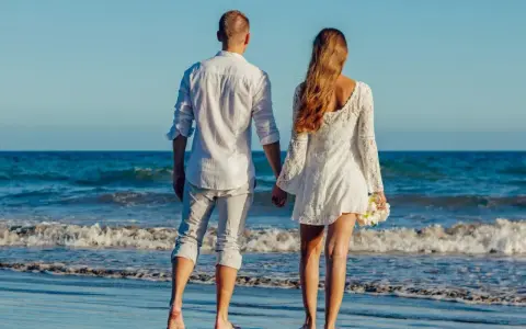 Para idąca plażą, trzymająca się za ręce. Ich miłość grecka kwitnie na tle błękitnego morza i nieba.