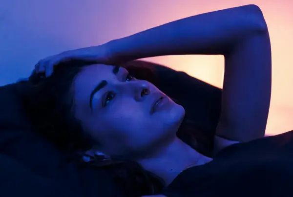 Młoda kobieta leży w łóżku, ręka oparta o głowę. Nocne światło tworzy intymną atmosferę, idealną na seks po kryjomu.